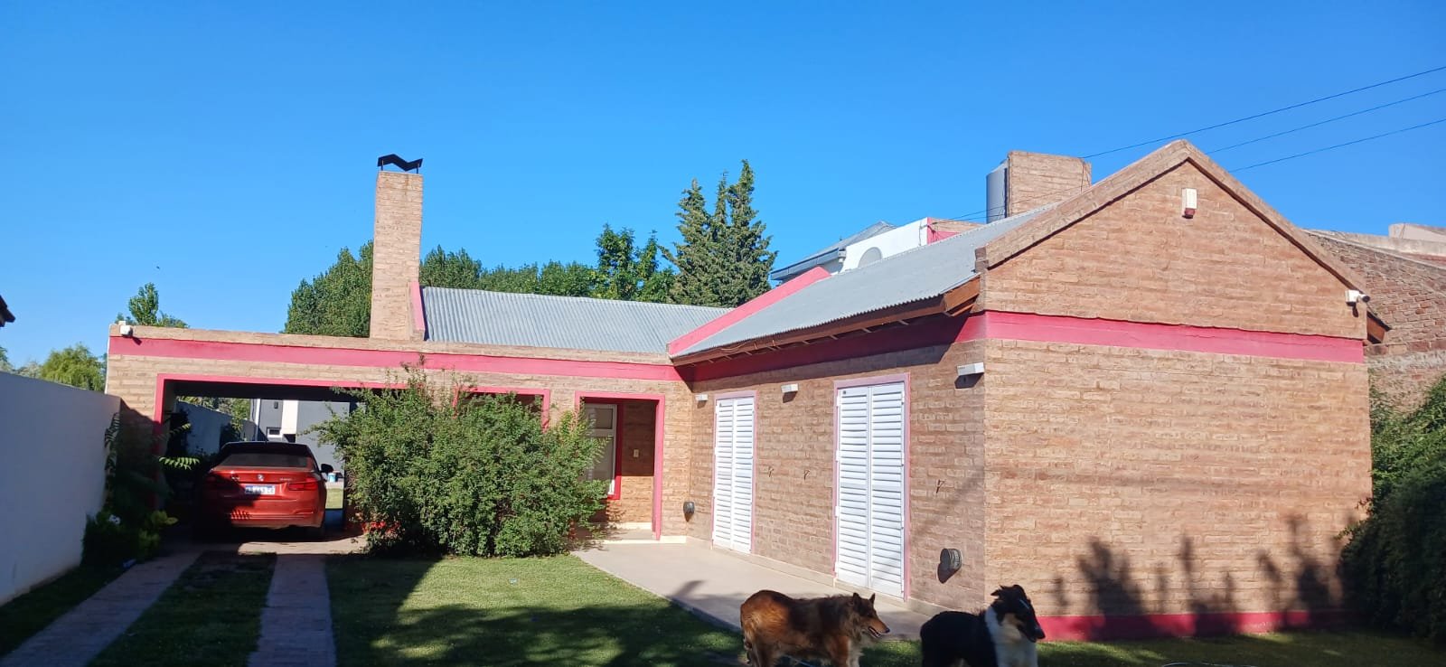 Fachada de casa de ladrillos con detalles rosas y cochera — proyecto CASA ANDREA, por Amorosi Espacios de Diseño, en Neuquén